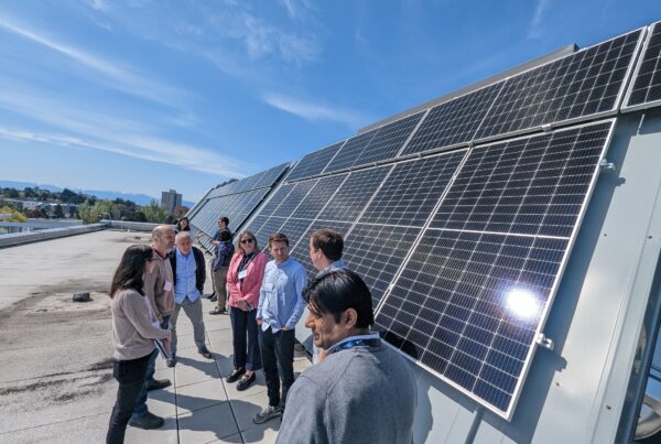 People standing on a rooftop next to solar panels under a blue sky.
