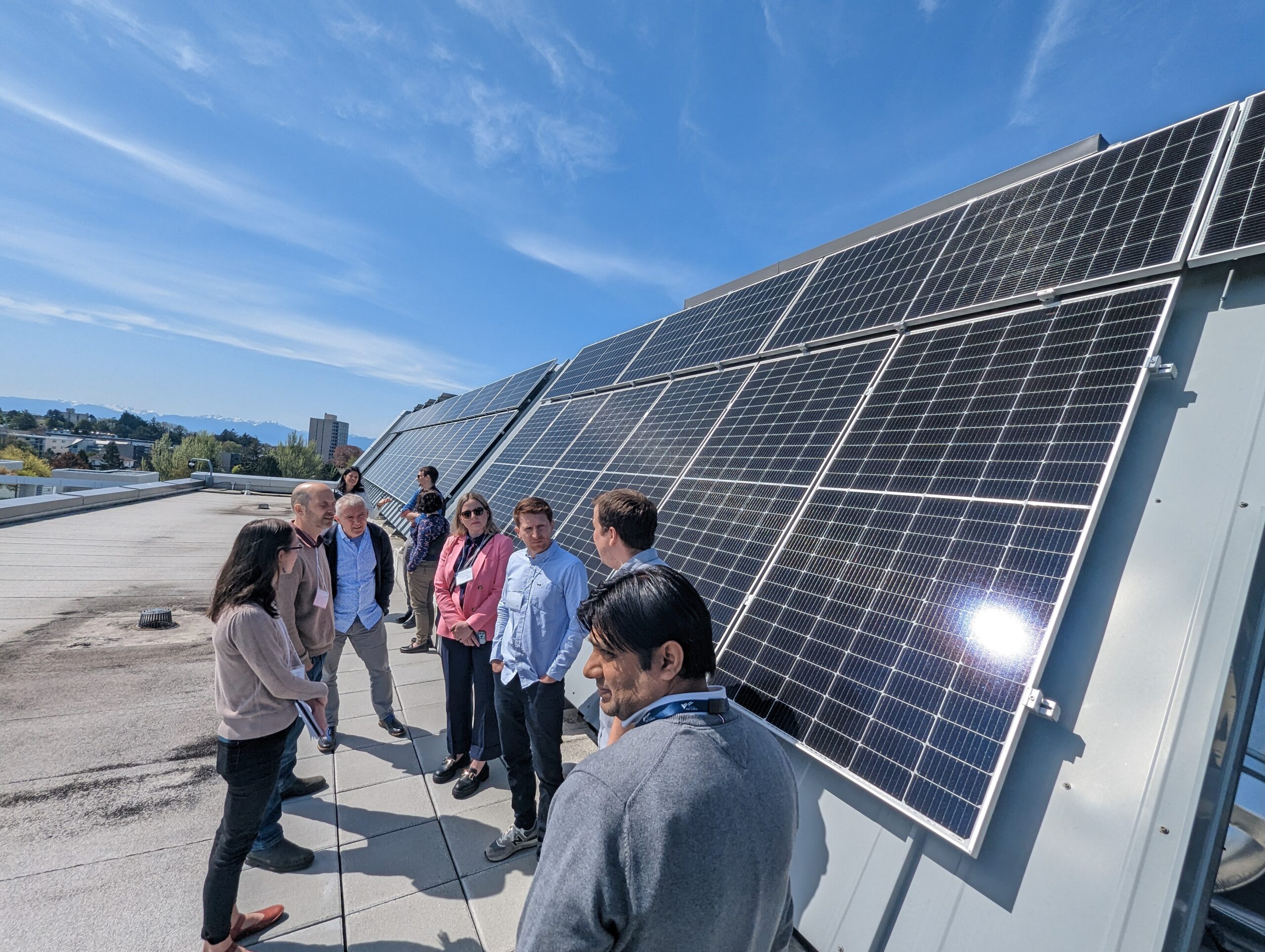 People standing on a rooftop next to solar panels under a blue sky.
